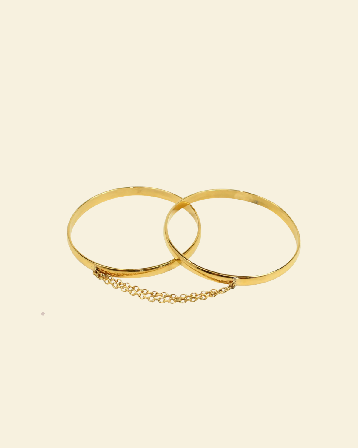 Two gold bangles with a chain on a beige background