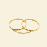 Two gold bangles with a chain on a beige background