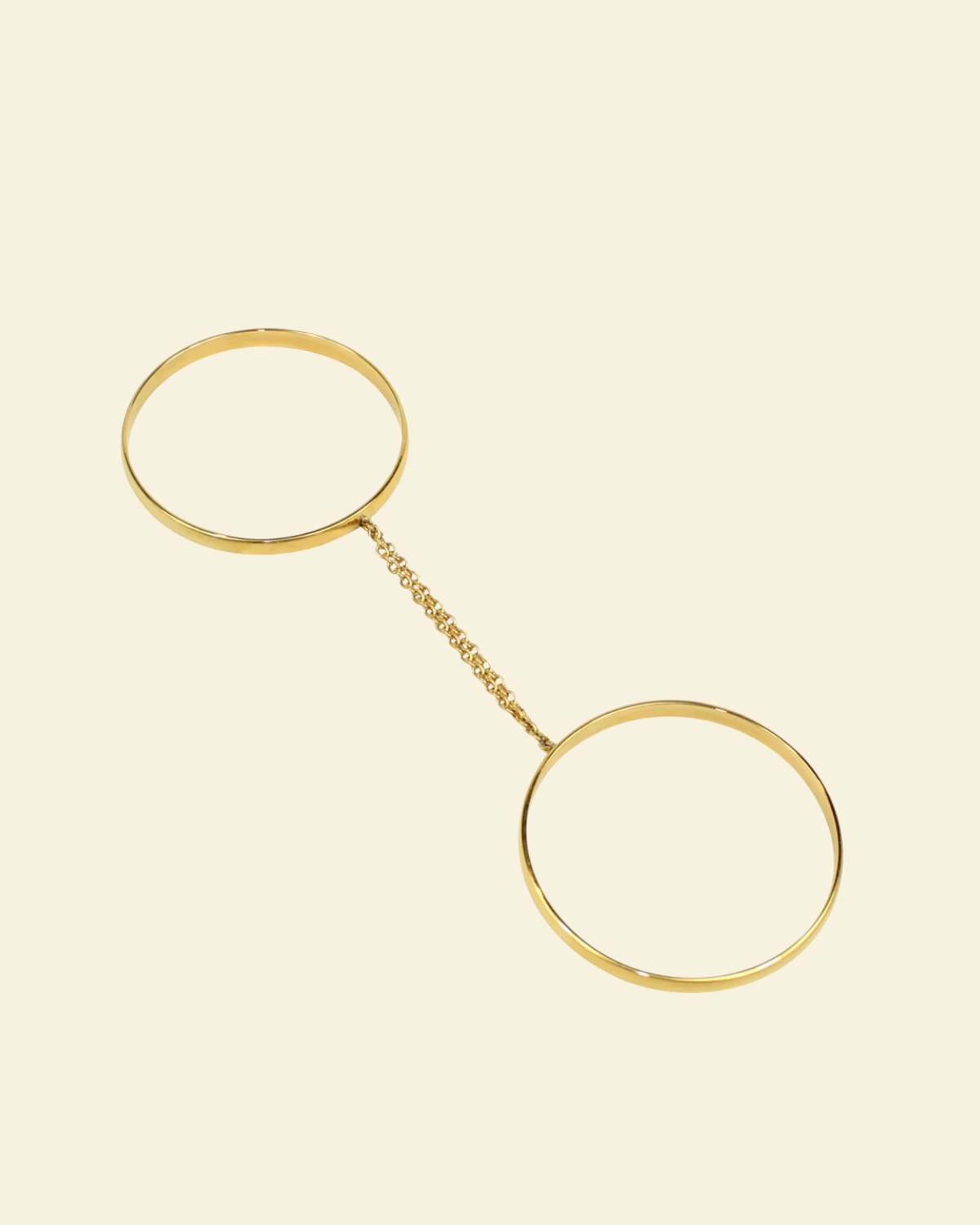Gold bracelet with two circular ends on a beige background