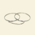 Two silver bangles with a chain on a beige background