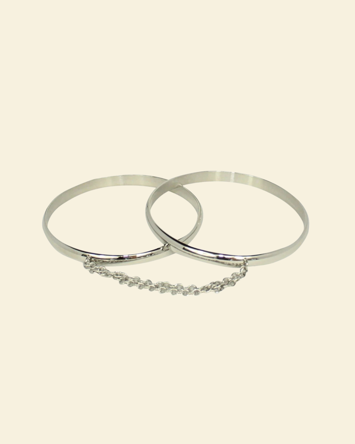 Two silver bangles with a chain on a beige background