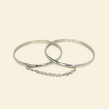 Two silver bangles with a chain on a beige background