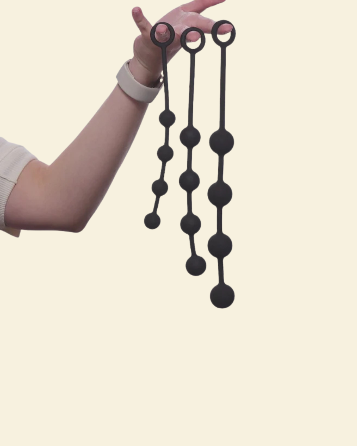 A hand holding 3 black anal beads in varying sizes