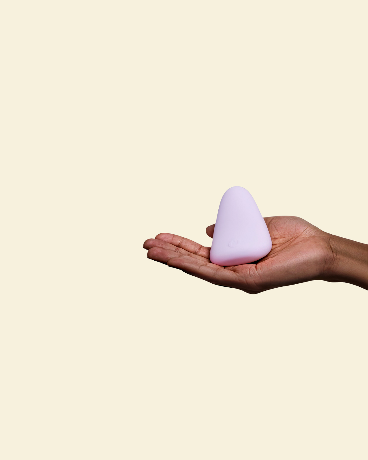 Purple silicone palm vibrator held in a hand on a beige back ground