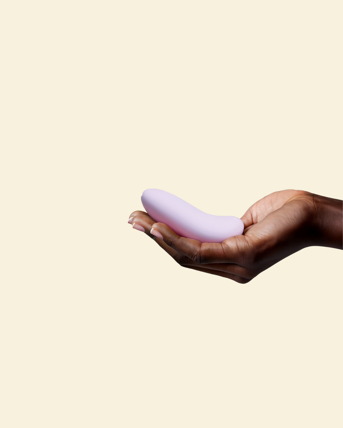 Hand holding a purple silicone palm vibrator on a beige background