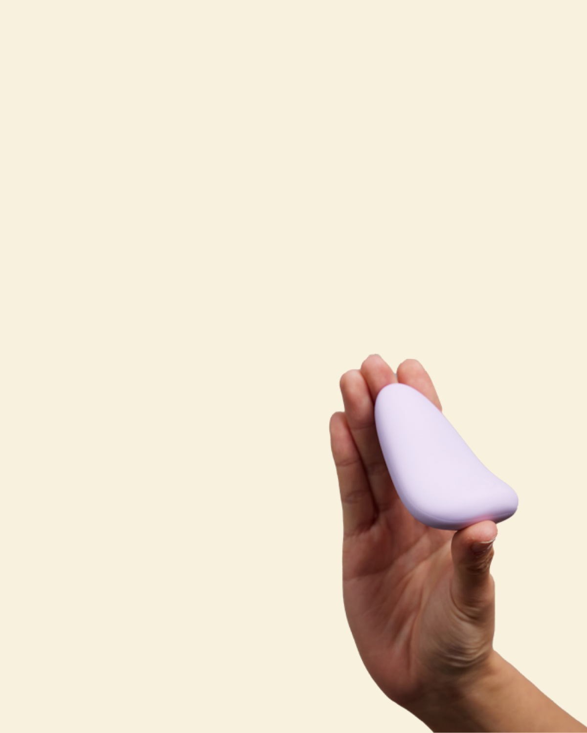 Hand holding a purple silicone palm vibrator against a beige background