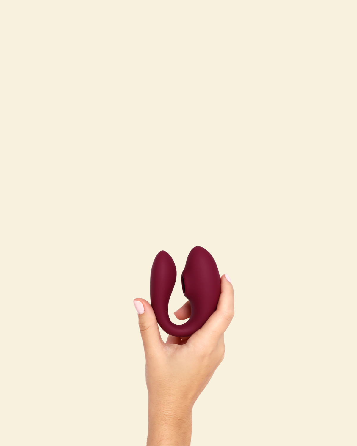 Hand holding a plum colored blended stimulation vibrator on a beige background