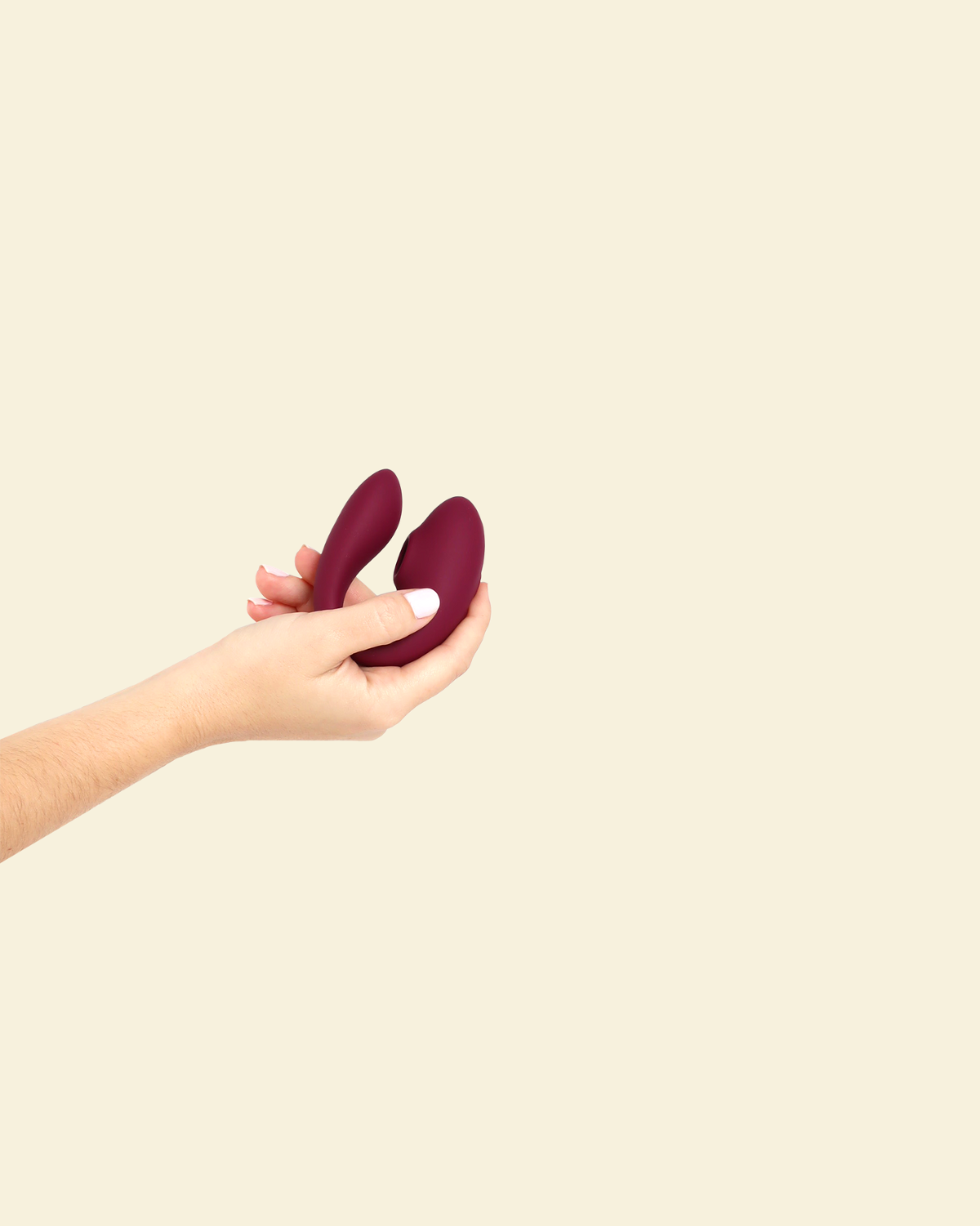 Hand holding the plum colored blended stimulation vibrator on a beige background
