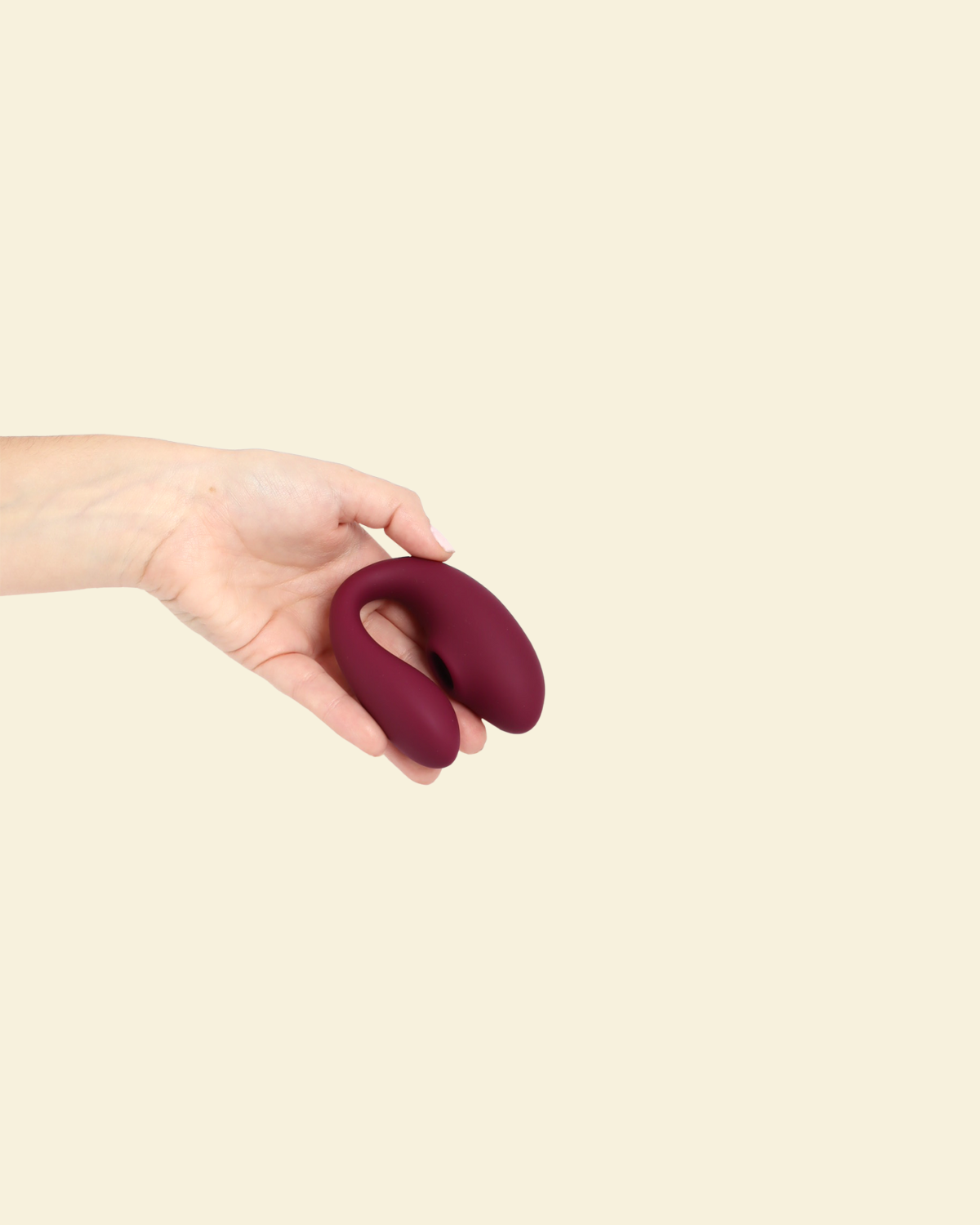 Hand holding the plum colored blended stimulation vibrator on a beige background