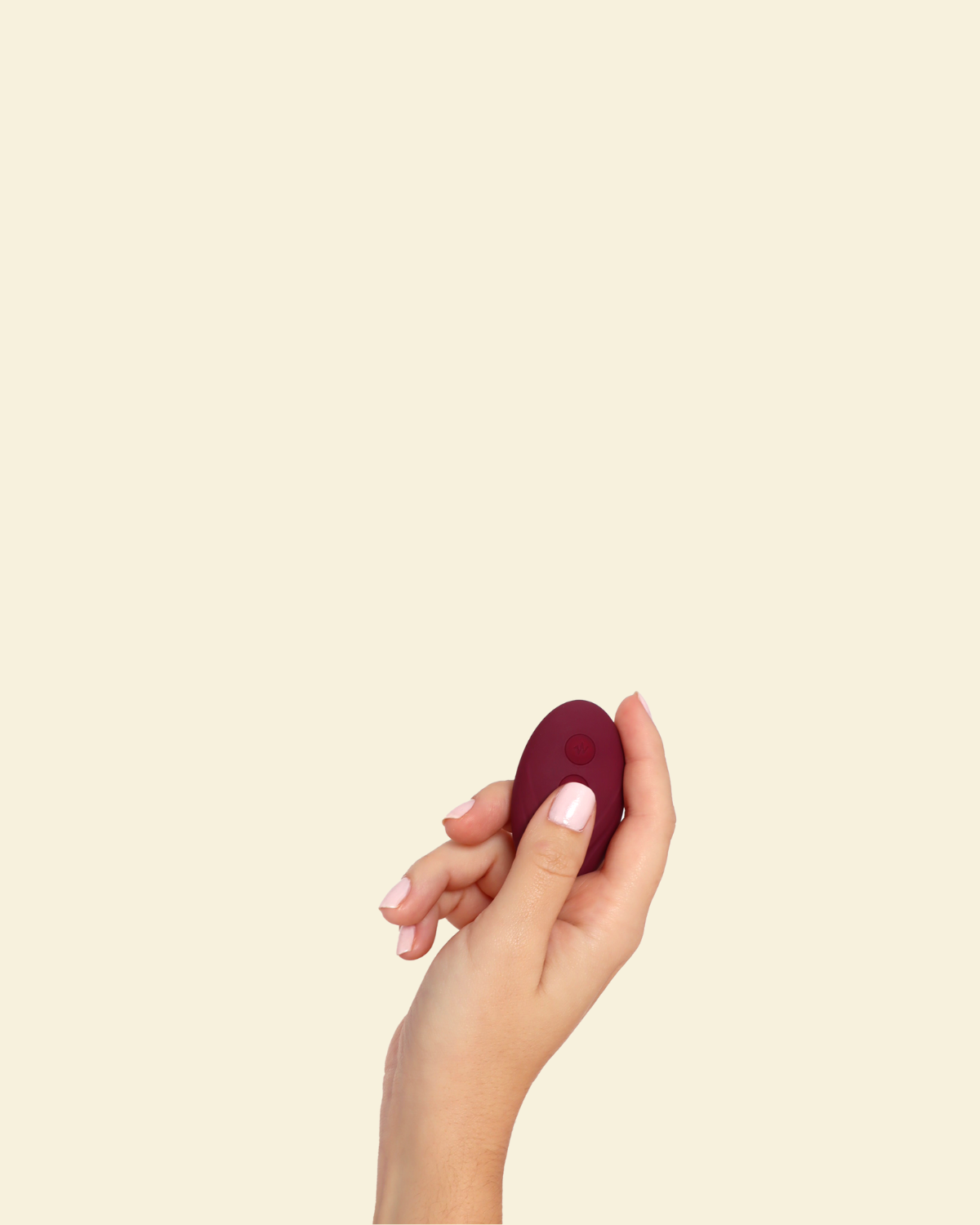 Hand holding the remote for the plum colored blended stimulation vibrator on a beige background