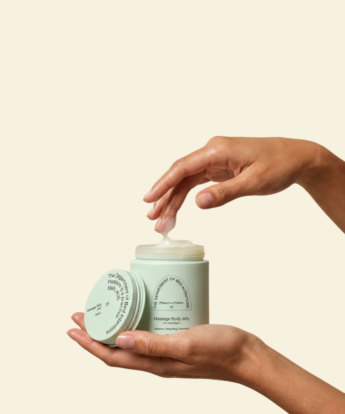 A person's hands holding an open jar of massage body butter with cream being dispensed, set against a solid light beige background.