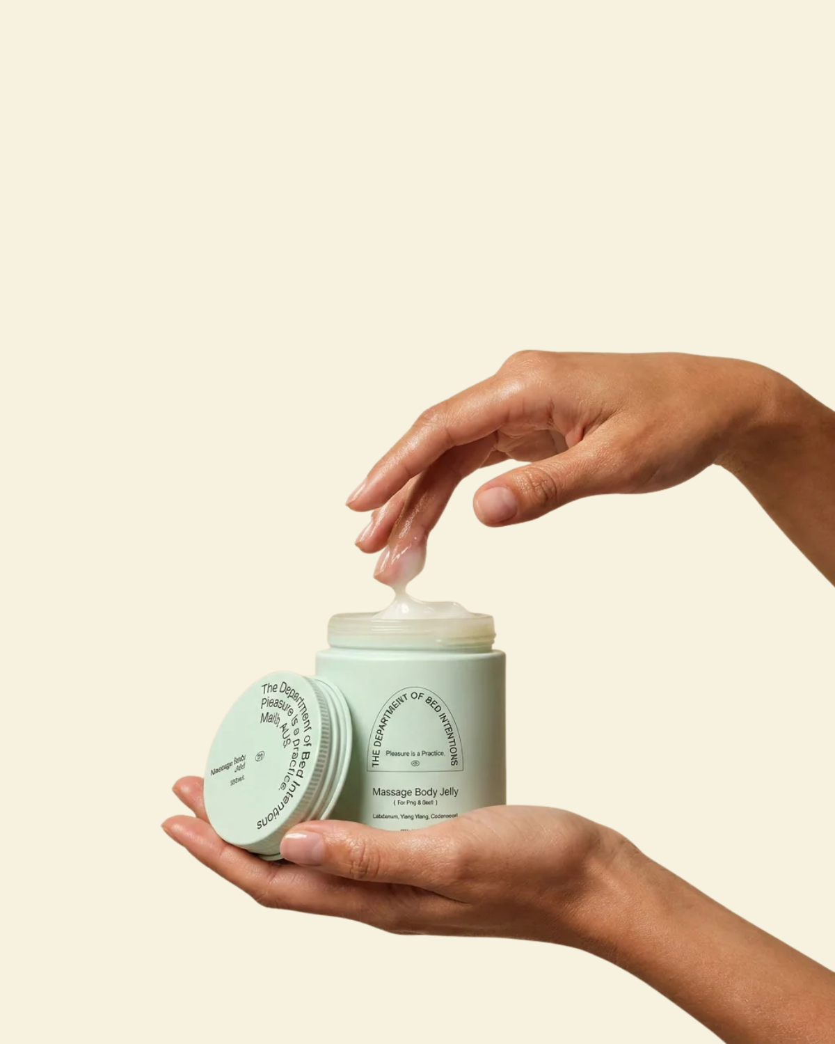 A person's hands holding an open jar of massage body butter with cream being dispensed, set against a solid light beige background.