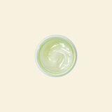 A top-down view of a small round container filled with a pale yellow-green cream or gel, centered on a solid light beige background.