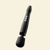 A black wand massager with a flexible silicone bulb attachment, featuring three white control buttons on the handle, shown against a solid pale cream background.