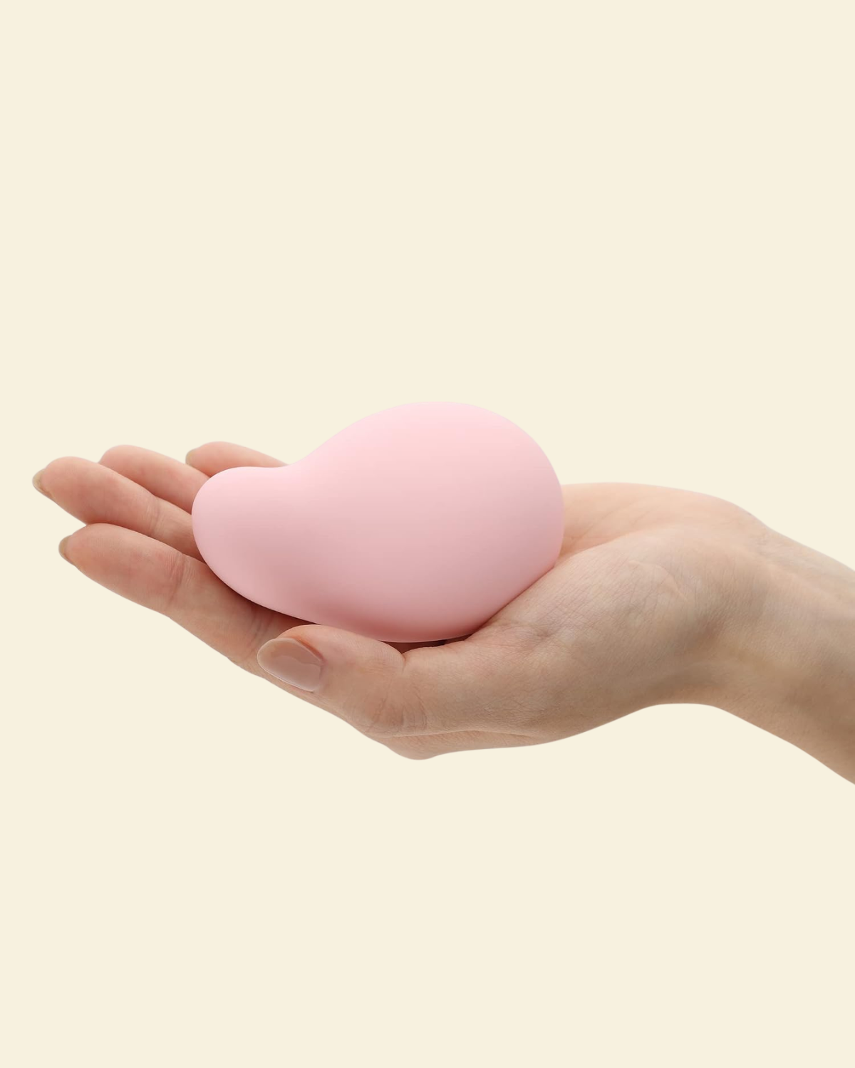 A hand holding a soft pink palm vibrator by Tenga Iroha