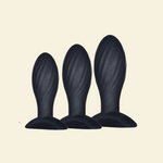 Three black silicone butt plugs of different sizes on a beige background