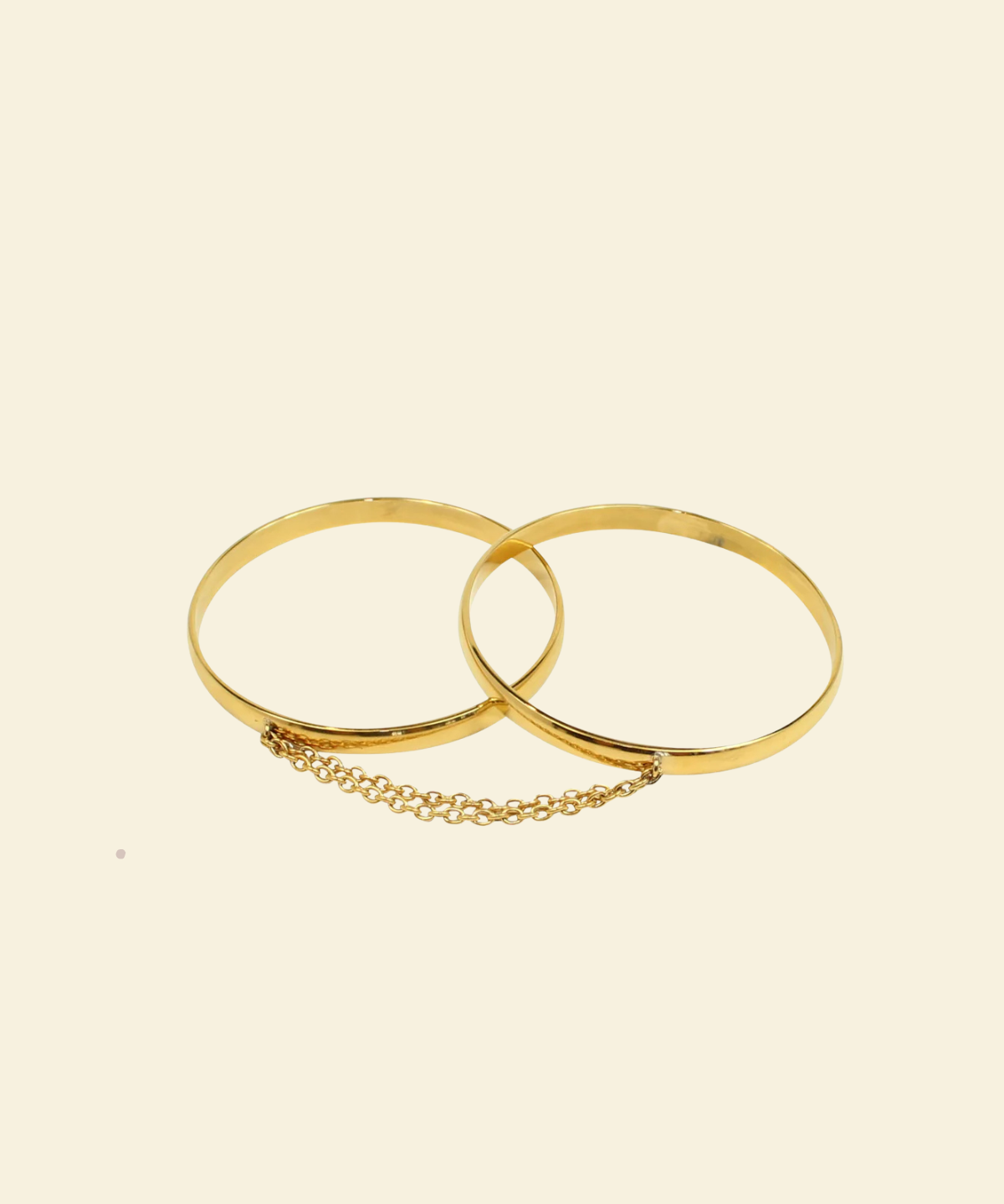 Two gold bangles with a chain on a beige background