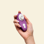 Hand holding a purple Womanizer Air suction toy on beige background