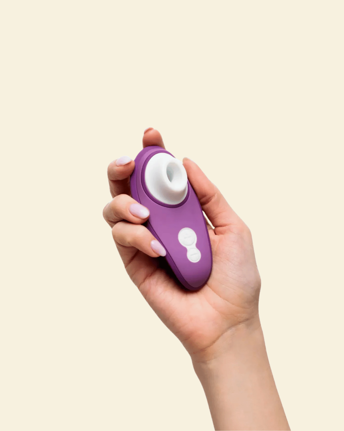 Hand holding a purple Womanizer Air suction toy on beige background