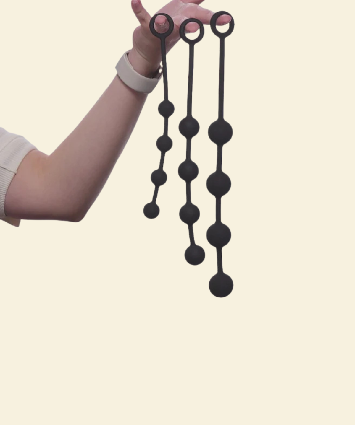 A hand holding 3 black anal beads in varying sizes