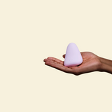 Purple silicone palm vibrator held in a hand on a beige back ground