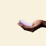 Hand holding a purple silicone palm vibrator on a beige background