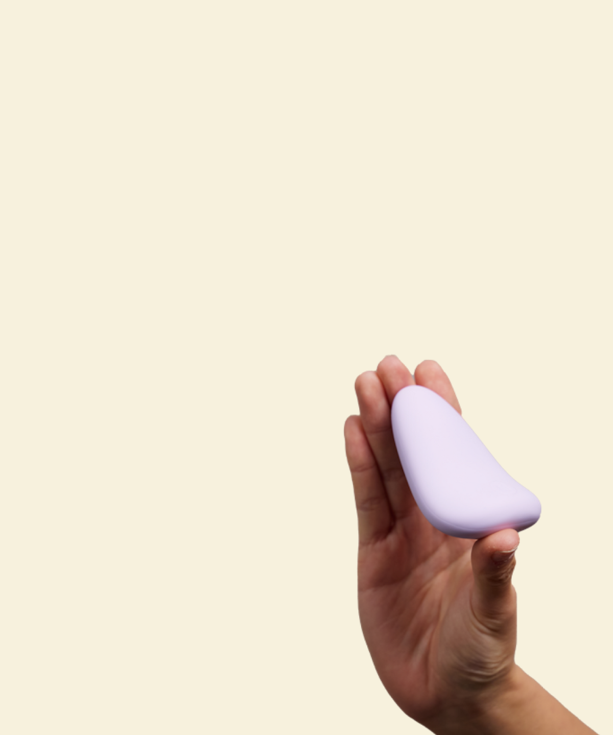 Hand holding a purple silicone palm vibrator against a beige background