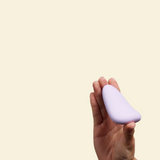 Hand holding a purple silicone palm vibrator against a beige background
