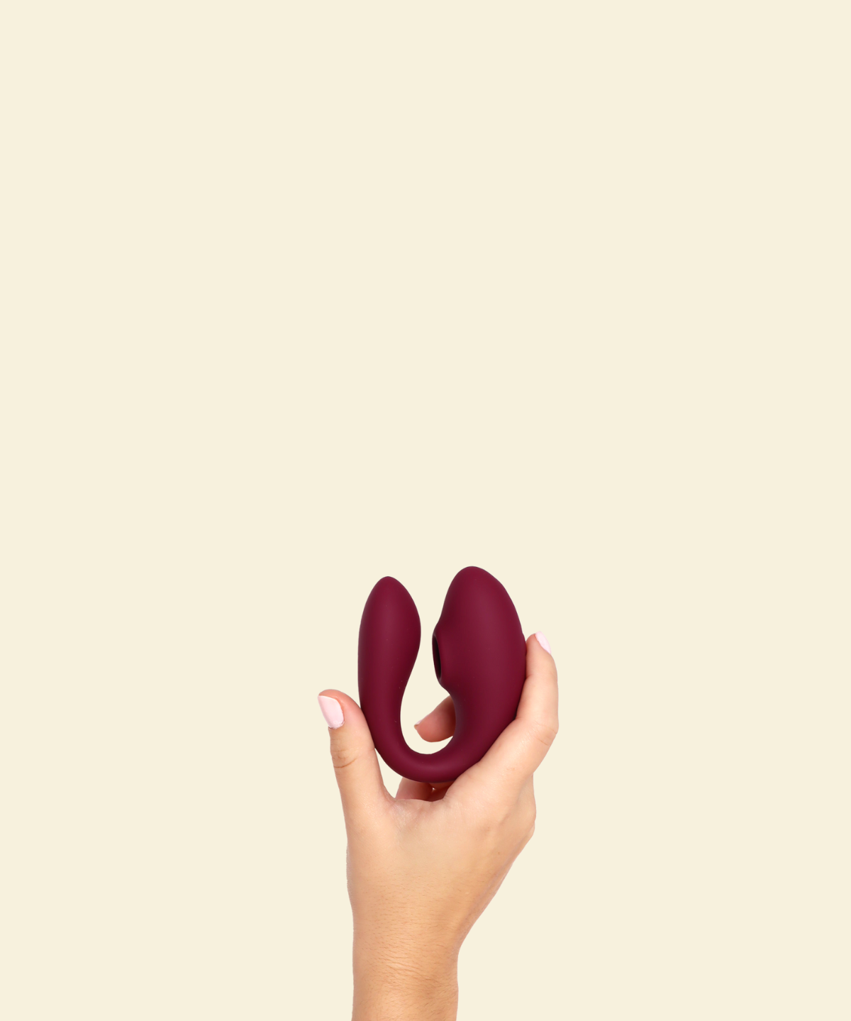Hand holding a plum colored blended stimulation vibrator on a beige background