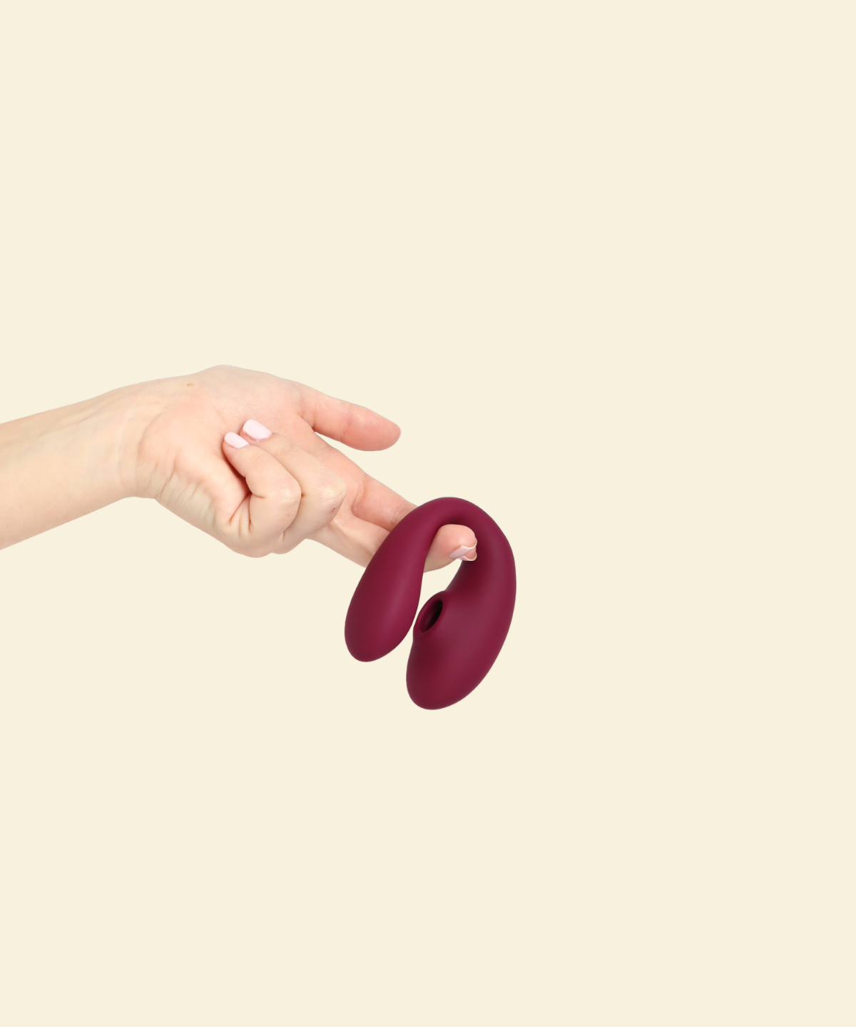 Hand holding the plum colored blended stimulation vibrator on a beige background