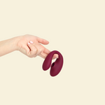 Hand holding the plum colored blended stimulation vibrator on a beige background
