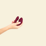 Hand holding the plum colored blended stimulation vibrator on a beige background