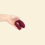 Hand holding the plum colored blended stimulation vibrator on a beige background