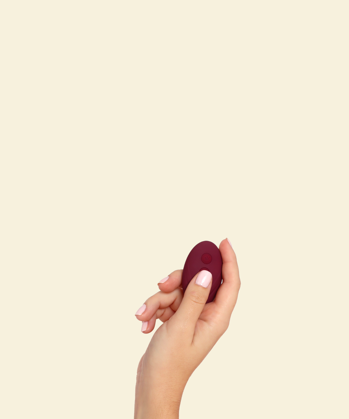 Hand holding the remote for the plum colored blended stimulation vibrator on a beige background