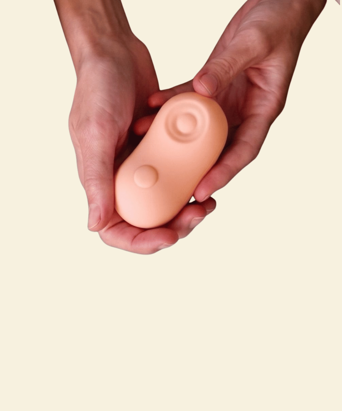 Two hands holding a coral colored tapping and vibrating massager 