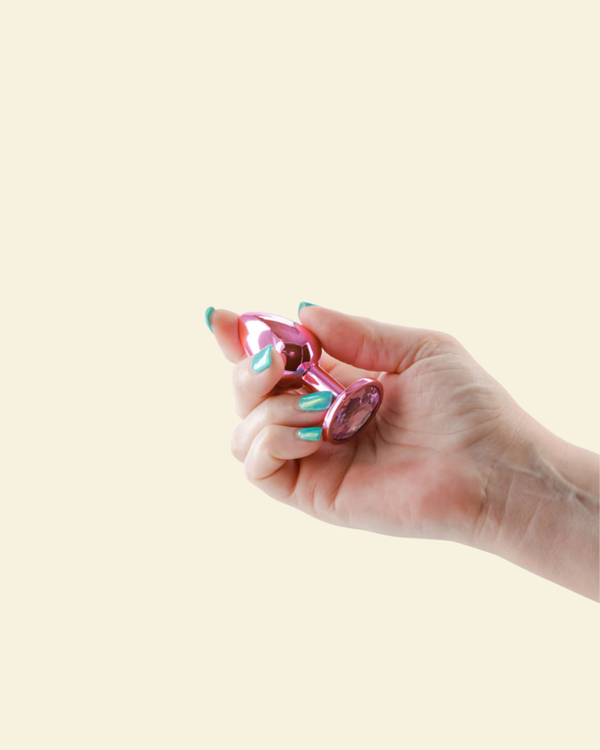 Hand holding a pink butt plug against a beige background