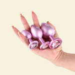 Hand holding 3 different sizes pink butt plugs