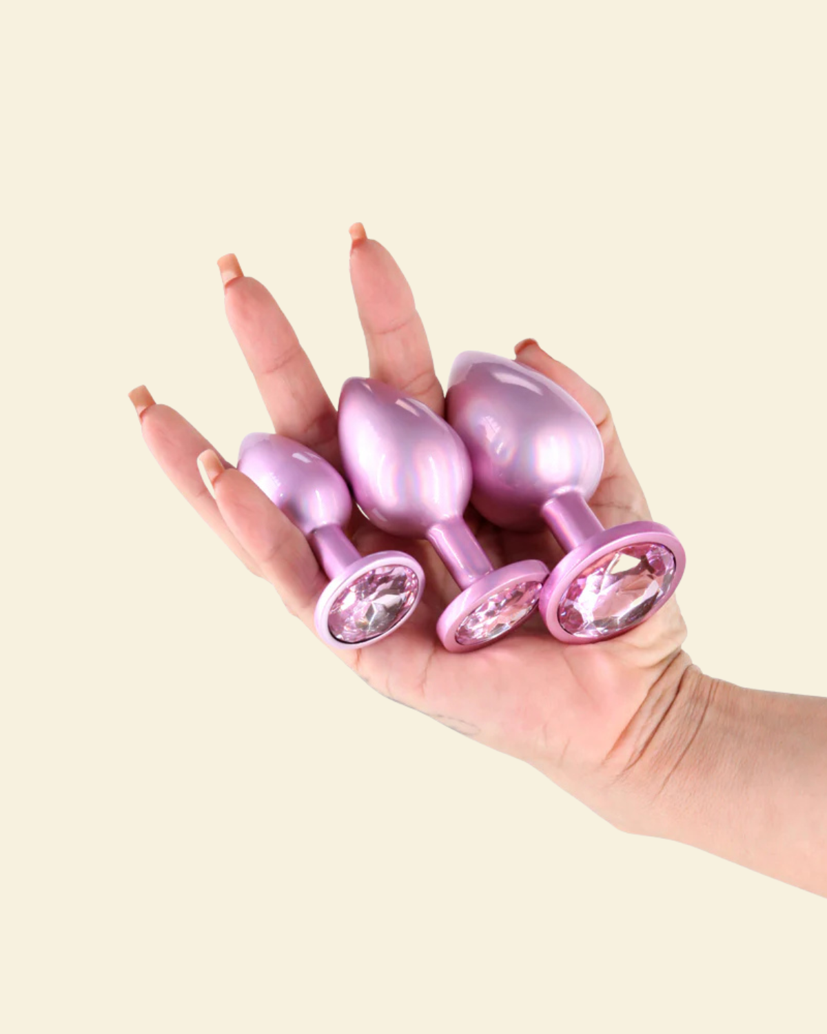 Hand holding 3 different sizes pink butt plugs