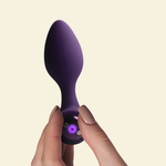 A hand holding a purple silicone vibrating butt plug