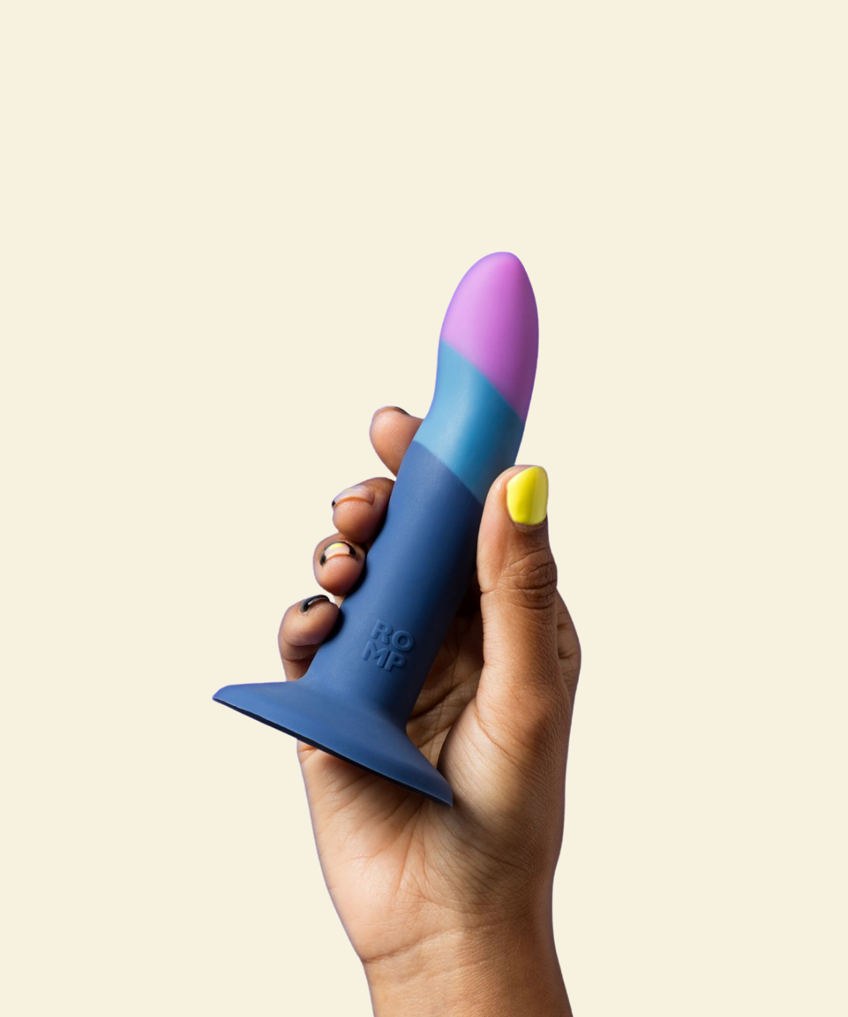 Hand holding a blue and purple silicone dildo against a beige background