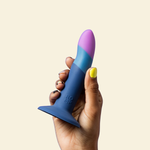 Hand holding a blue and purple silicone dildo against a beige background