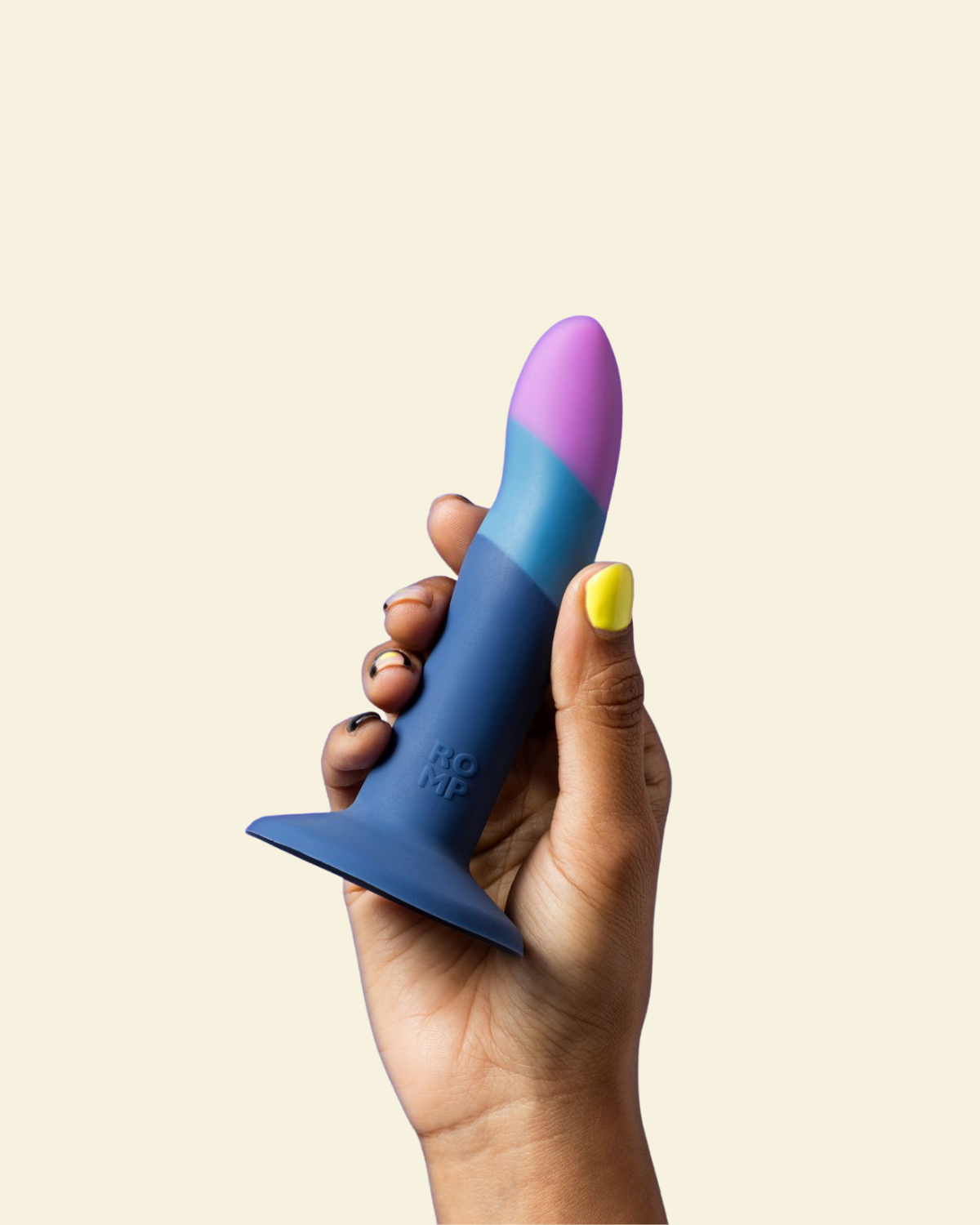 Hand holding a blue and purple silicone dildo against a beige background