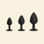 Three black silicone butt plugs of different sizes on a beige background