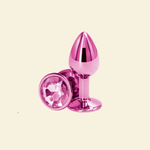 Pink metallic anal plug with a gemstone on a beige background