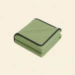 Folded matcha green waterproof blanket with black trim on a beige background