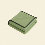 Folded matcha green waterproof blanket with black trim on a beige background