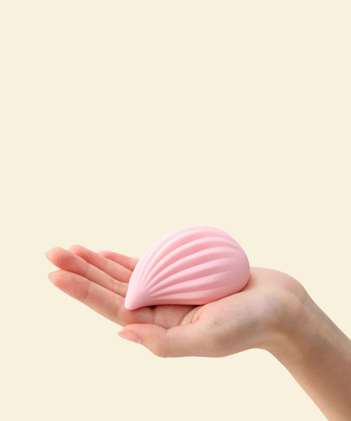 Pink shell-shaped object held in a hand against a beige background