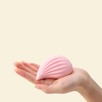 Pink shell-shaped object held in a hand against a beige background