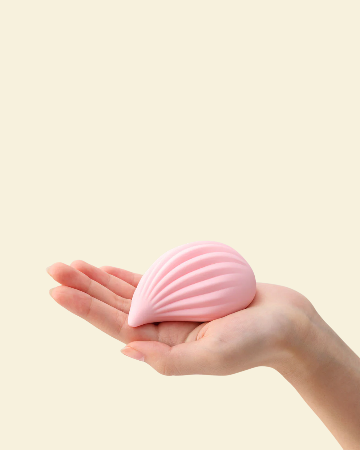 Pink shell-shaped object held in a hand against a beige background