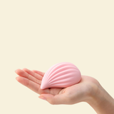 Pink shell-shaped object held in a hand against a beige background